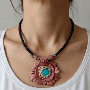 A handcrafted bohemian choker necklace displayed on a woman's neck, featuring a flower design made of pink-brown leather petals with a blue turquoise stone in the center and a black braided cord.